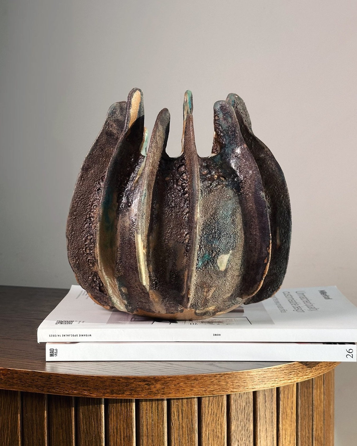 Clutch claw-like stoneware vessel styled on a wood side table with books